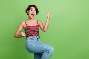 Photo of crazy lovely cheerful glad girl wear trendy clothes raise hands fist yell yes isolated on green color background