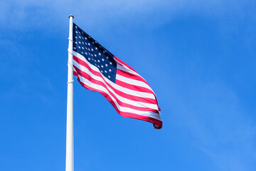 large american flag waving in wind on a pole against blue sky, patriot and independence holidays