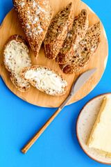 Bread on cutting board with butter on plate, slice of bread with butter on blue background top view