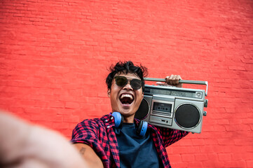 Smiling young man with boombox celebrates life. Vibrant street culture shines against a red wall backdrop. Energy and retro vibes in urban setting.