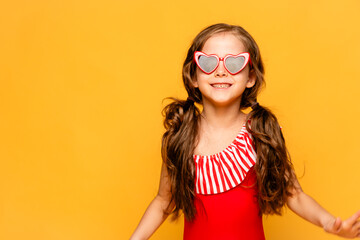 A beautiful cute little girl in a red swimsuit and sunglasses laughs cheerfully on yellow background. Mock up. Summer vacation concept. Place for text. Advertising of children's products and sale