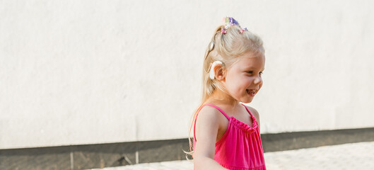 Banner child girl walks and have fun outdoor with cochlear implant on the head. Hearing aid and...