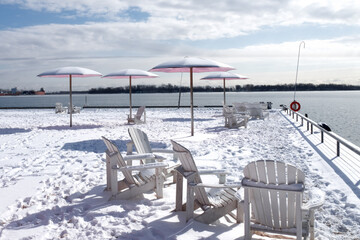 Naklejka premium pink umbrellas and white Adirondak chairs at a waterfront park covered in snow in winter