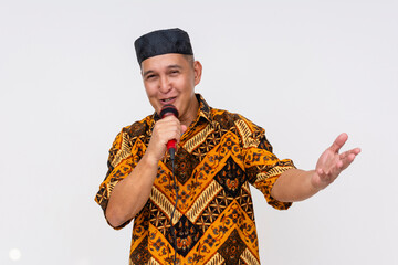 An Indonesian man in a traditional batik shirt and kopiah hat emceeing, with a microphone, isolated...