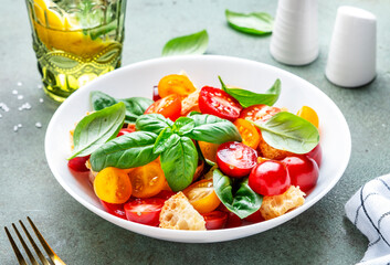 Simple italian salad with with stale bread, cherry tomatoes, olive oil, sea salt and green basil white plate, stone table background, top view