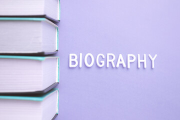 A stack of books with biography written on the cover in electric blue and magenta tints and shades. The font is bold and the rectangle pattern is printed on wood with a brand logo