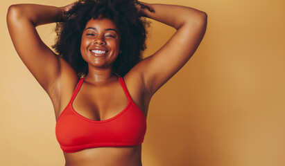 A radiant woman in a red top enjoys a carefree moment, her hands in her curly hair, embodying confidence and self-positivity against a warm backdrop.