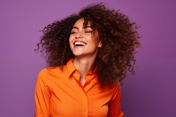 A woman in a bright orange top is the epitome of exuberance, her hair wildly flowing, with a contagious laugh set against a vibrant purple backdrop.