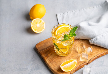 Iced drink with lemon, mint in a glass on a wooden board on a light background with citrus fruits.