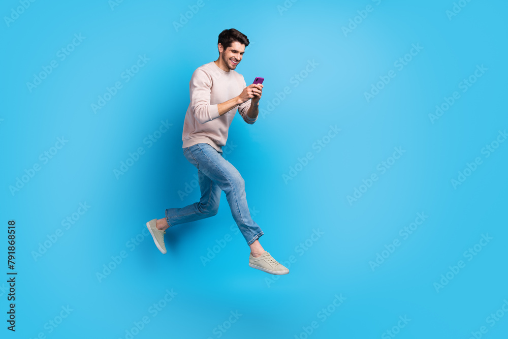 Poster full length photo of optimistic cheerful guy wear pullover fast running with smartphone in hands iso