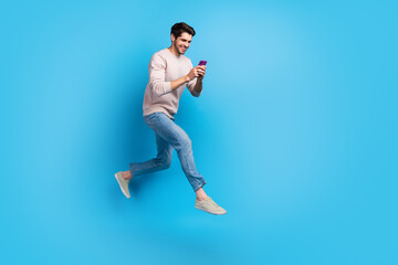 Full length photo of optimistic cheerful guy wear pullover fast running with smartphone in hands...
