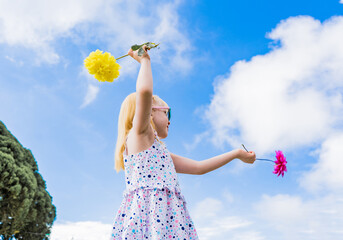 niña albina jugando al aire libre con sus manos en el aire y sosteniendo flores de  colores  - obrazy, fototapety, plakaty