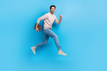 Obraz premium Full size photo of optimistic cheerful man wear sweatshirt denim pants run to empty space with laptop isolated on blue color background