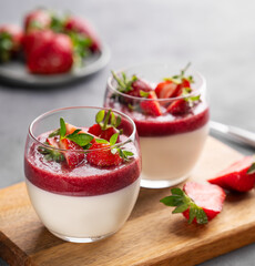 Strawberry and cream panna cotta in glasses with fresh berries on a wooden board on a gray...