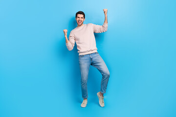 Full length photo of lucky excited man wear beige sweatshirt rising fists screaming isolated blue...