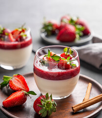 Strawberry and cream panna cotta in glasses with fresh berries on a wooden plate on a light background with cinammon close up