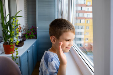 A cute boy looks out the window of a balcony, waves to his friends and laughs. The boy is standing...