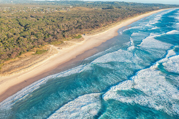 Patterned foamy ocean waves roll in and approach sandy beach. Majesty turquoise sea. Top view drone.