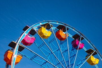 Colorful ferris wheel on a fairground in California. Orange, yellow and pink gondola cabins isolated on blue sky. Historic amusement park “Boardwalk“ on the beach of Santa Cruz, California (USA)