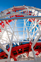 Wooden roller coaster at a funfair. Colorful red and white painted historic wooden structure of a waterfront amusement ride in Santa Cruz, California (USA). Wide angle low angle view on a sunny day.