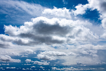 Cloudscape on a sunny day with white and gray cloud formations, hidden sun and blue sky. Wide angle shot on a day with nice weather. 