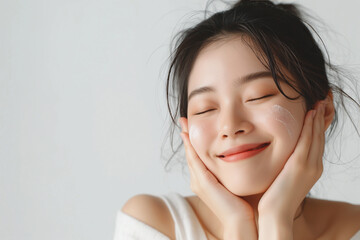 A so beautiful korean beauty model woman in her thirties smiling and touching the skin on her face with both hands, eyes closed, wearing white against a plain light background