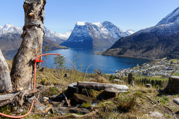 Overlooking a tranquil fjord, snow-capped mountains rise majestically behind a peaceful village....
