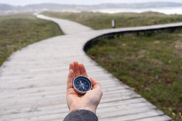 A person holding a compass on a wooden boardwalk. The promenade has two paths. - obrazy, fototapety, plakaty