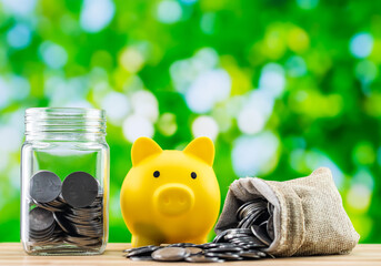 A glass jar and a yellow piggy bank along with a sack full of coins.