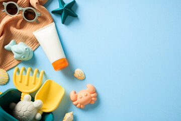 Baby sunscreen in tube, towel, sunglasses, bucket with sand molds on blue background. Flat lay, top view, copy space.