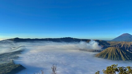 Bromo volcano during the dawn, East Java, with a mountain and flowing fog layer.