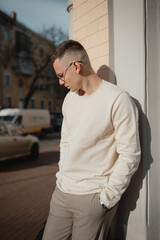 Fototapeta premium handsome young male businessman of model appearance in stylish clothes and glasses posing for the camera. A business guy in a sweater walks around the city in good summer weather