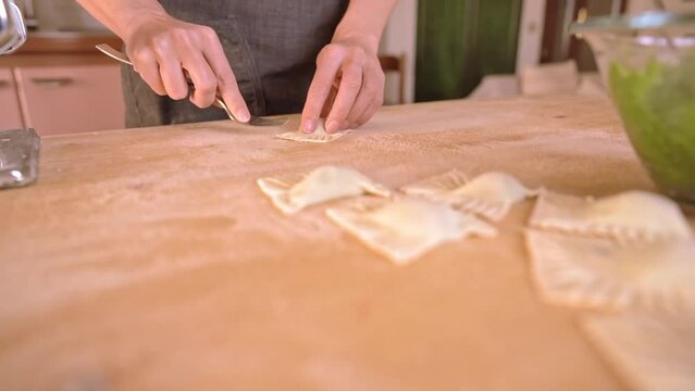 4k slow motion process of homemade vegan Italian recipe tortelli or ravioli filled with vegetables. Woman chef seals the edges with a fork on the wooden work table and poses in close-up to the camera.