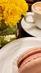 Vase with yellow flowers, sweet macaroon and coffee cup