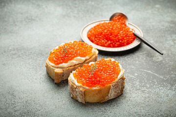 Small metal plate with red salmon caviar and two caviar toasts canape on grey concrete background, festive luxury delicacy and appetizer.