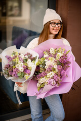 Colorful flowers in the hands of a cheerful girl who stands in a sweater and jeans - 791927121