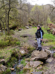 Young photographer standing on a large rock in a forest woodland scene with a slow moving moorland stream surrounded by trees