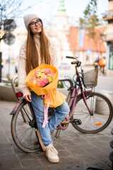 Smile on a face of a girl in hat stands near a bicycle on a city street