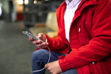 Close up picture of a guy with phone in hands sitting on the bench