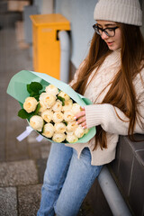Dark-haired girl in knitted hat sweater with a bouquet of beautiful roses