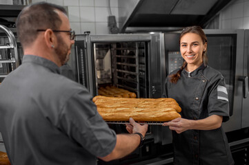 Colleagues working in a bakery and holding a tray with fresh buns