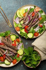 Two plates with traditional Thai beef salad with vegetables and mint top view served on rustic concrete background, healthy exotic asian meal.