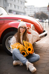 Yellow sunflower in hands of a girl sitting near a vintage car