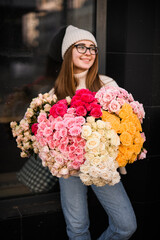 Perky girl in light sweater and jeans stands with a bouquet of colorful flowers - 791934579