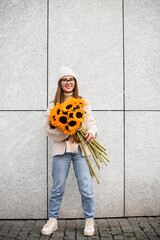Sunflowers in a hands of a girl in glasses who stands near wall