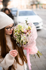 Girl with fair skin in a glasses standing on a city street with a large bouquet