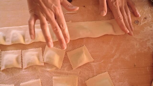 4k slow motion top down view of the cook wife's hands pressing with fingers and cutting the strip of filled pasta with the wheel to shape ravioli or green tortelli. Traditional homemade food recipe