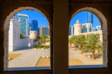 View through arched windows at Qasr Al Hosn fort of the historic Arabic castle and modern skyline of Abu Dhabi, United Arab Emirates.