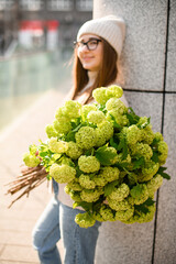 Smiling girl with brown hair in a knitted sweater and hat with a bouquet of flowers - 791937303