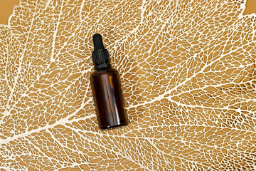 Blank amber glass essential oil bottle on podium stand on golden line leaf texture. Skin care...